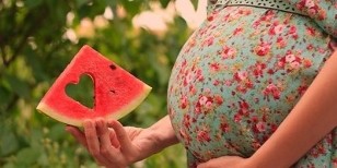 Rebanada de sandía en la mano de una mujer embarazada